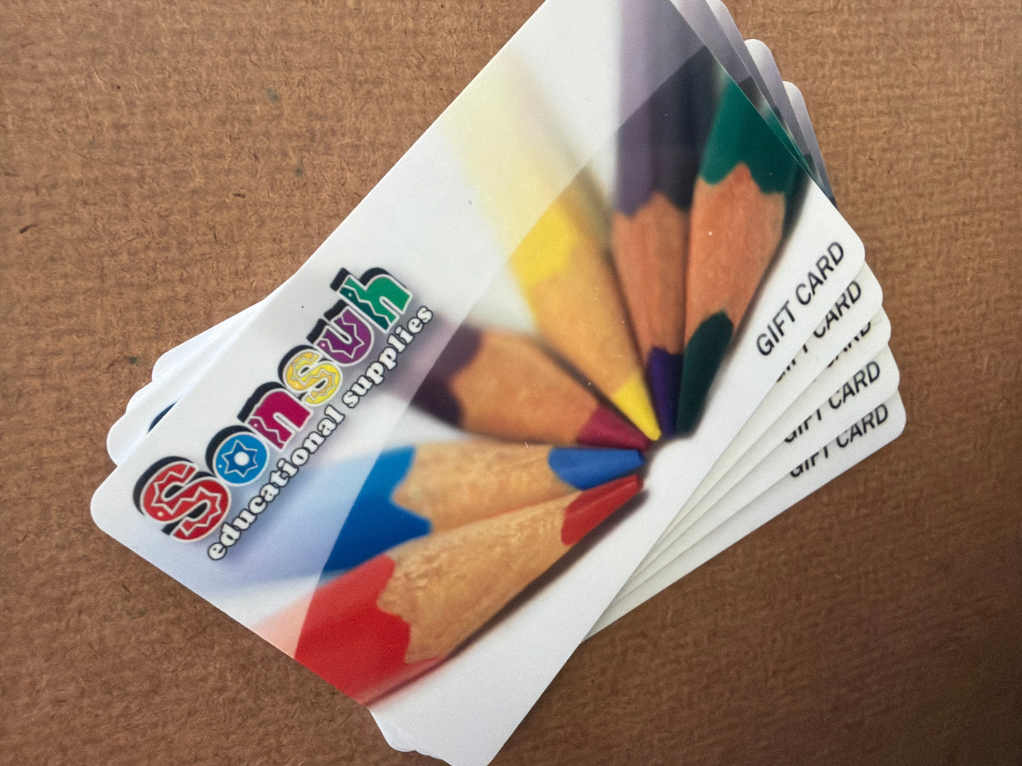 Gift cards with colorful pencils and 'Sensuh Educational Supplies' branding on a brown background